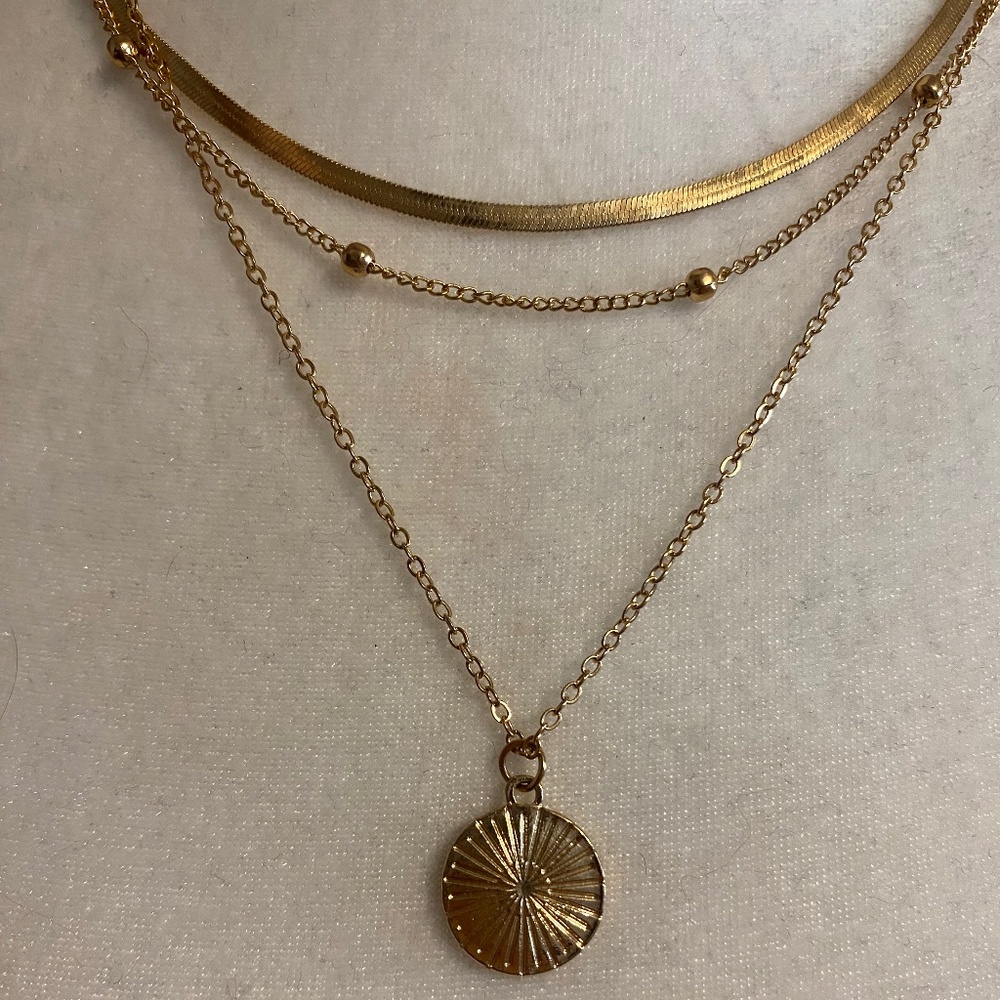 Gold toned three strand single clasp layered necklace.